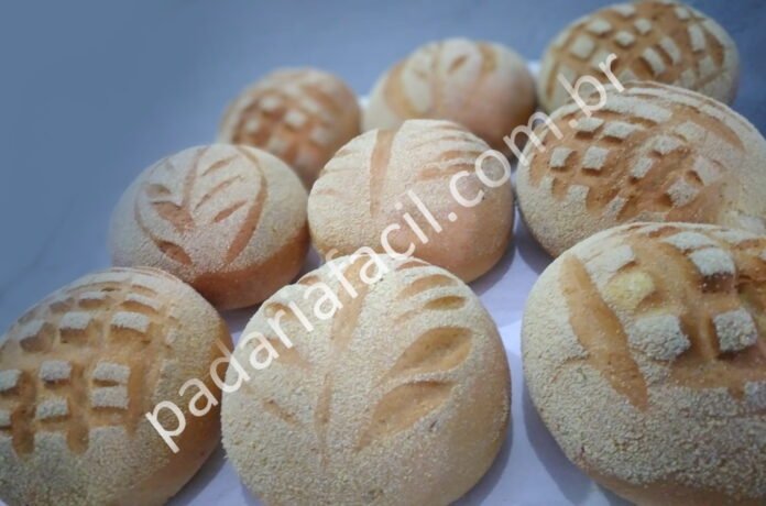 Imagem com a foto de nove pães broas de milho redondos, com enfeiteis feitos com pequenos cortes na superfície dos pães, e todos polvilhados com farinha de milho.