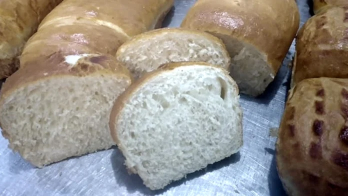 Imagem com a foto de cinco pães caseiros, sendo que um deles está cortado em fatias.