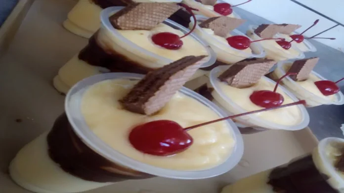 Copos plásticos transparentes com creme branco e de chocolate, enfeitados com cereja vermelha com talo e wafer.