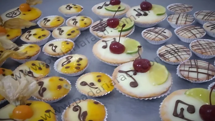 Várias tortinhas de limão e maracujá. As de limão pequenas estão com riscos finos de chocolate preto que formam uma grade, as de limão grande estão enfeitadas com símbolos musicais, meia fatia de limão e uma cereja com talo. As de maracujá pequenas, são enfeitadas com uma geleia amarela, sementes de maracujá e arabescos de chocolate. As grandes são enfeitadas com a mesma geleia amarela com sementes de maracujá, ,as com um desenho de folha de planta feita de chocolates e uma physalis natural.